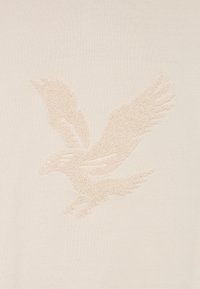 Diepe reliëf van een adelaar met uitgespreide vleugels in lichtbeige textiel op een bijpassende gladde achtergrond.