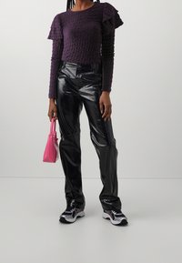 Lila texturerad långärmad topp med volanger vid axlarna, i kombination med glansiga svarta byxor och en liten rosa handväska. Sneakerna har en flerfärgad design.