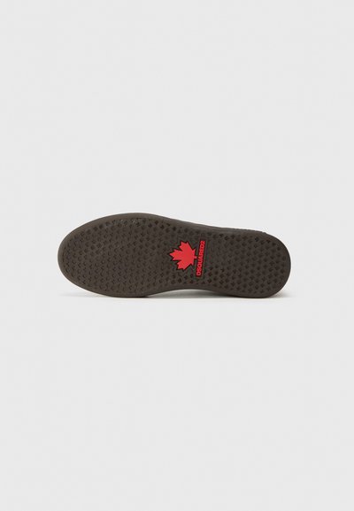 Semelle de chaussure en caoutchouc noir avec une surface texturée et de petits motifs circulaires. Logo de feuille d'érable rouge avec "DSQUARED2" imprimé près du talon.