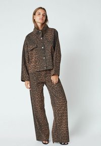 Brown leopard print denim jacket with matching wide-leg pants. Features a pointed collar, front buttons, and a relaxed fit. Black open-toed shoes.
