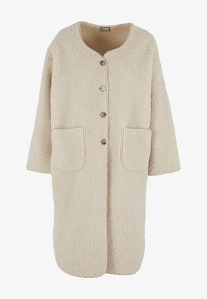 Beige faux bontjas met een ronde halslijn, sluiting met knopen aan de voorkant, korte mouwen en twee zakken. Zachte textuur en losse pasvorm.