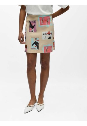 Beżowa mini spódnica z kolorowym, abstrakcyjnym i figuralnym wzorem, noszona z białymi butami na niskim obcasie w szpic oraz białą bluzką.