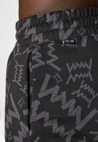Nærbilde av svarte joggebukser med grå abstrakte sik-sak mønstre og elastisk liv med et lite sydd merke.