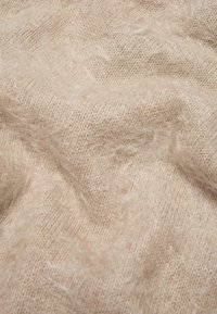 Tessuto a maglia beige chiaro con una texture morbida e pelosa. I fili sono sottili e intrecciati in modo lasco, creando un aspetto confortevole.