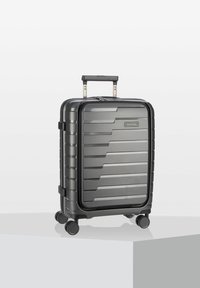 Valigia nera rigida con scanalature orizzontali, manico retrattile e quattro ruote per la mobilità. Chiusura con zip e etichetta del marchio visibile.