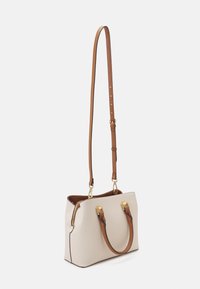 Beżowa torebka z brązowymi skórzanymi elementami, wyposażona w podwójne górne uchwyty i regulowany pasek. Gładka faktura i detale w złotym kolorze.