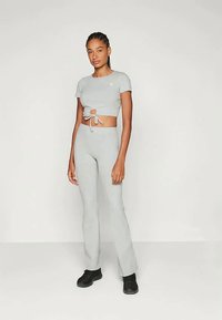 Šviesiai pilkas dviejų dalių kostiumas, sudarytas iš trumpų marškinėlių su raišteliu ir aukšto liemens plačių kelnių, pagamintas iš minkštos medžiagos.