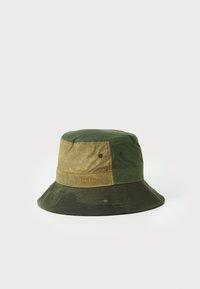 Groene en beige emmerhoed met een bicolor ontwerp, gemaakt van duurzaam materiaal, met gestikte accenten en een logolabel aan de zijkant.