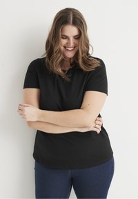 Zwarte T-shirt met korte mouwen en een ronde halslijn, gecombineerd met donkere spijkerbroek. Zachte stof met een relaxte pasvorm en een subtiele glans.