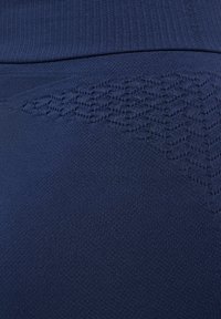 Navy blauwe legging close-up, met een textuur patroon langs de bovenkant, gemaakt van een rekbare stof met een gladde afwerking.