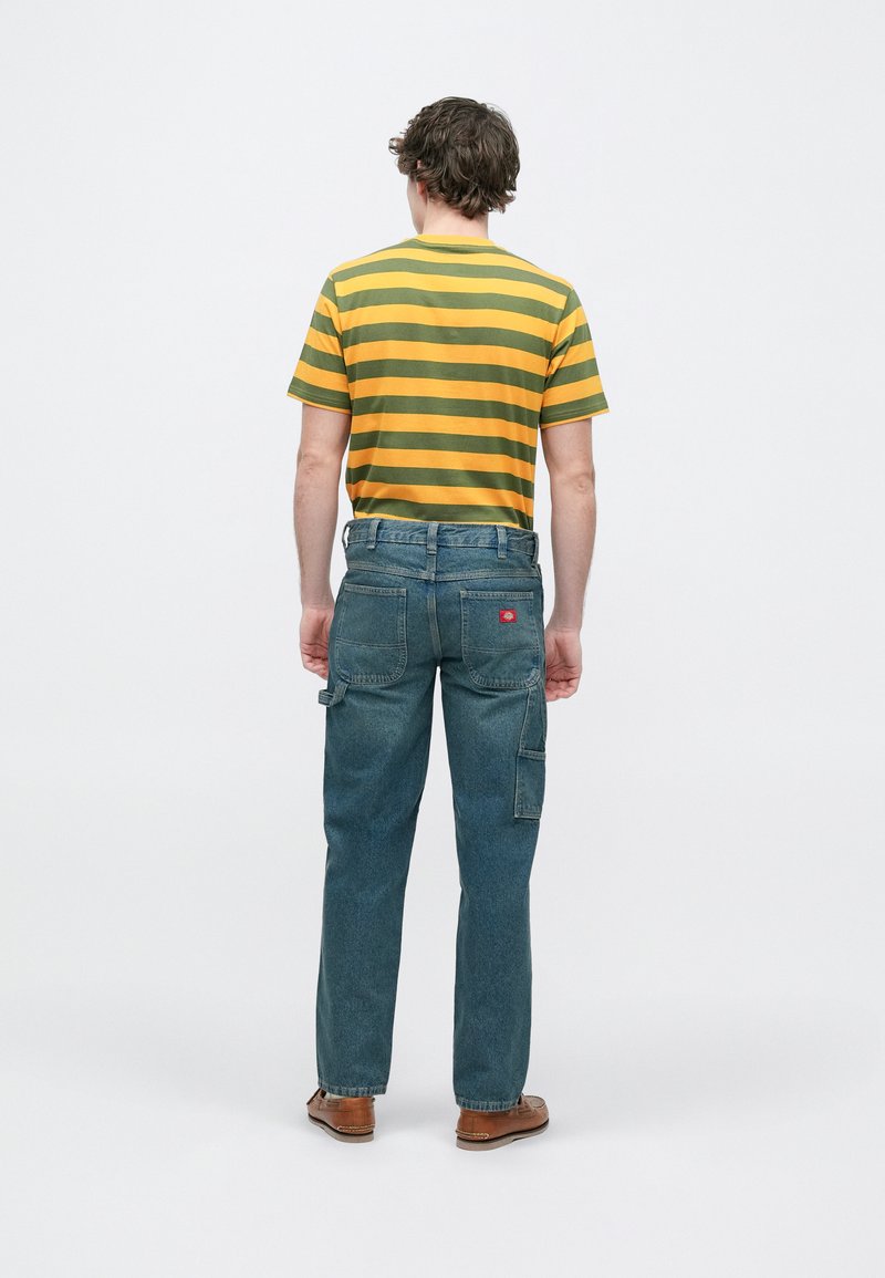 Maglietta a maniche corte a righe gialle e verdi con scollatura tonda; abbinata a pantaloni cargo di jeans blu con tasche laterali e etichetta rossa.