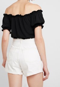 Top negro sin hombros con mangas acampanadas, combinado con pantalones cortos blancos de tiro alto con dobladillos enrollados y bolsillos traseros.