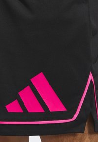 Mustat urheilushortsit, joissa on teksturoitu kangas ja vaaleanpunaisia yksityiskohtia, mukaan lukien kolmiraita-logo ja vaaleanpunaiset kaitaleet helman ympärillä.