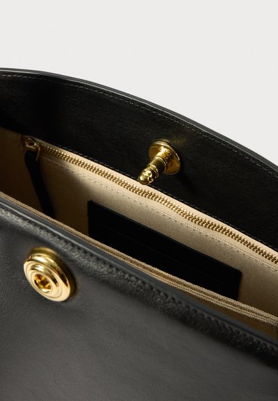 Unutrašnjost crne kožne torbe s bež tkaninom, zlatnim zatvaračem i zlatnim preklopom, s vidljivim detaljima šivanja.