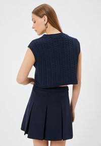 Marinblå kortärmad kabelstickad tröja som är cropped, kombinerad med en marinblå veckad kjol. Texturen är ribbad med ett vågigt mönster.