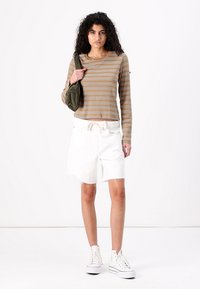 Chemise à rayures à manches longues en marron et beige, associée à un short blanc avec des ourlets effilochés et des baskets montantes blanches. Sac de couleur olive.