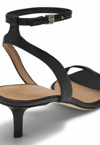 Black leather heeled sandals with thin ankle strap, a cushioned tan footbed, and a delicate heel. Features a silver buckle accent.