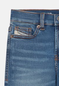 Vaqueros de mezclilla azul con un corte clásico, que presentan costuras naranjas, un pequeño bolsillo frontal y una etiqueta de marca visible dentro del bolsillo.
