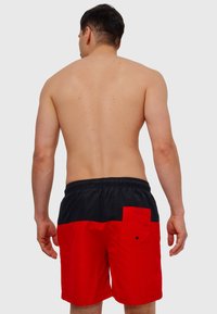 Røde og svarte svømmeshorts med elastisk midjebånd, med baklomme og kontrasterende fargeblokker. Glatt tekstur.