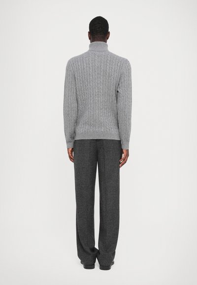 Grå strikket sweater med høj krave og kabelstrik, parret med løstsiddende mørkegrå bukser.