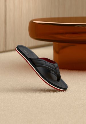 Tongs noires avec un accent rouge et blanc, présentant une texture mate lisse et une semelle contourée. Design léger, légèrement surélevé au-dessus de la surface.