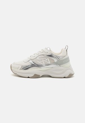 Sneakers atletici bianchi con accenti argentati lucidi, pannelli in rete e una suola spessa. Presenta un logo sul lato e un'etichetta sul tallone testurizzata.
