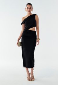 Must käeõlgne must kleit, millel on kortsus tekstuur ja lõike-detailid. Sile kangas, põrandapikkune, koos rihmadega kuldse tooni sandaalidega.