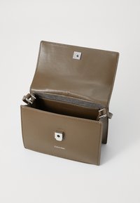 Sac à main en cuir marron avec un fermoir carré en métal argenté. Il dispose d'une seule sangle réglable et d'une texture lisse. À l'intérieur, il est doublé d'un tissu contrastant.