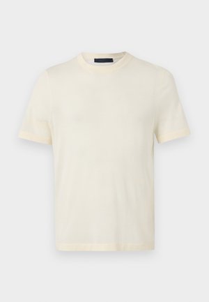 Camiseta de manga corta de color crema, con cuello redondo, diseño simple, exhibida sobre un fondo liso de color gris claro.