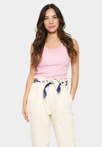 Pink ribbed tank top paired with beige high-waisted trousers, accented by a patterned blue and white belt. Model stands facing forward.