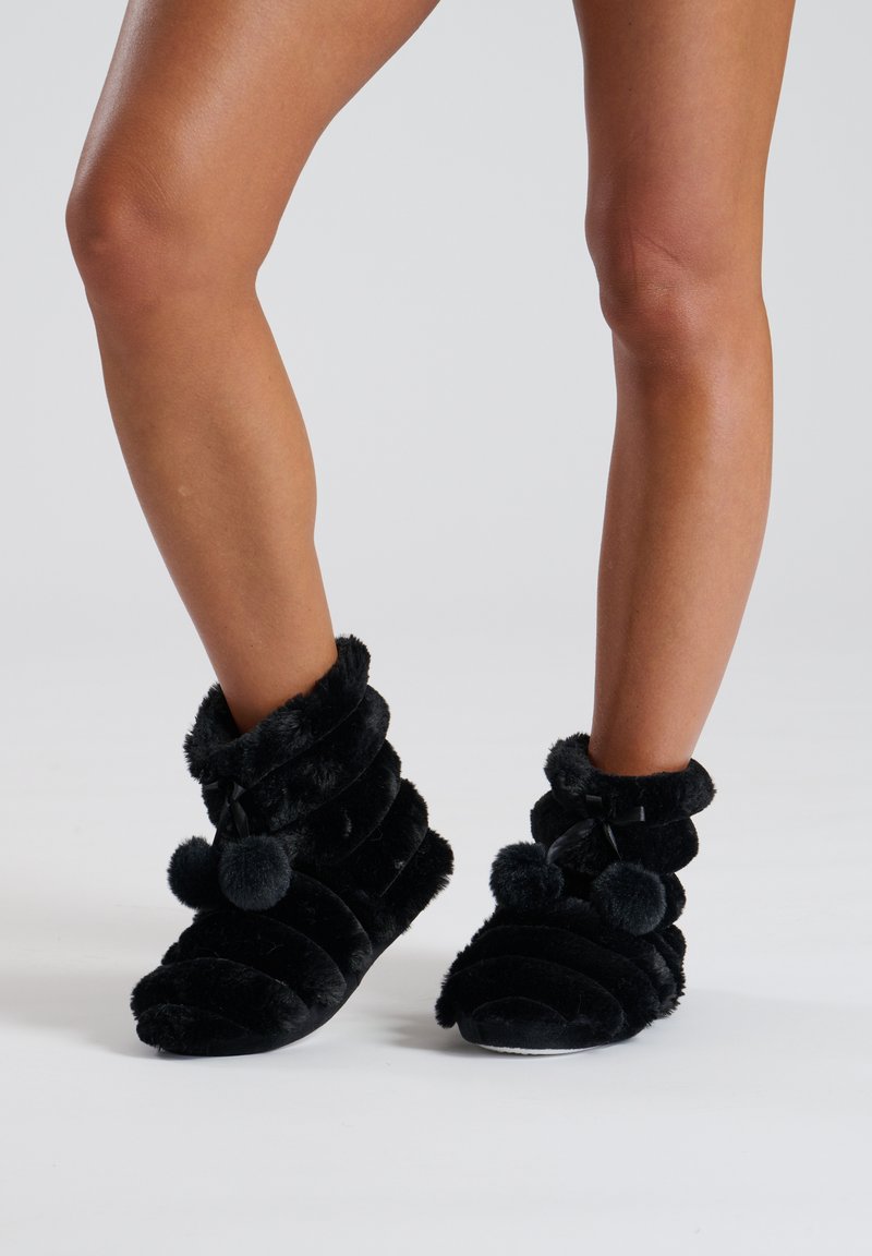 Black plush ankle boots with a ribbed design, pom-pom accents, and soft texture. Features a folded cuff for added comfort.