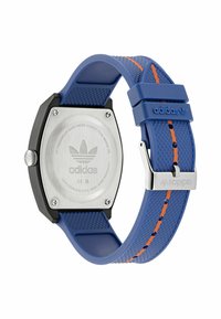 Montre rectangulaire bleu en silicone avec boîtier en acier inoxydable noir, bracelet texturé et bande orange. Présente le logo Adidas et un fermoir en métal.