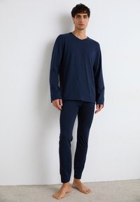 Navyblaues langärmeliges V-Ausschnitt-Oberteil und eng anliegende Hose aus weichem Stoff mit kontrastierenden Seitenstreifen entlang der Beine. Minimalistisches Design.