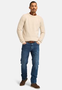 Maglione beige a costine, jeans in denim blu, cintura in pelle marrone e scarpe marroni. L'outfit presenta una vestibilità casual e rilassata con scollo rotondo.