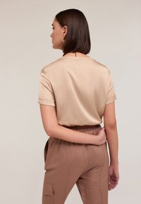 Beige satin top med korte ærmer og rund halsudskæring, parret med brune bukser med elastik i livet og sidelommer.