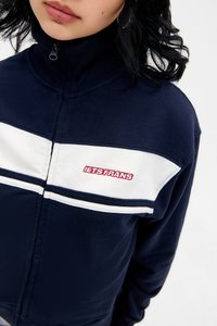 Marineblaue Zip-Jacke mit weißen und grauen Streifen über der Brust. Mit gesticktem "LETS FRANS" in Rot auf der linken Seite. Weicher Stoff.