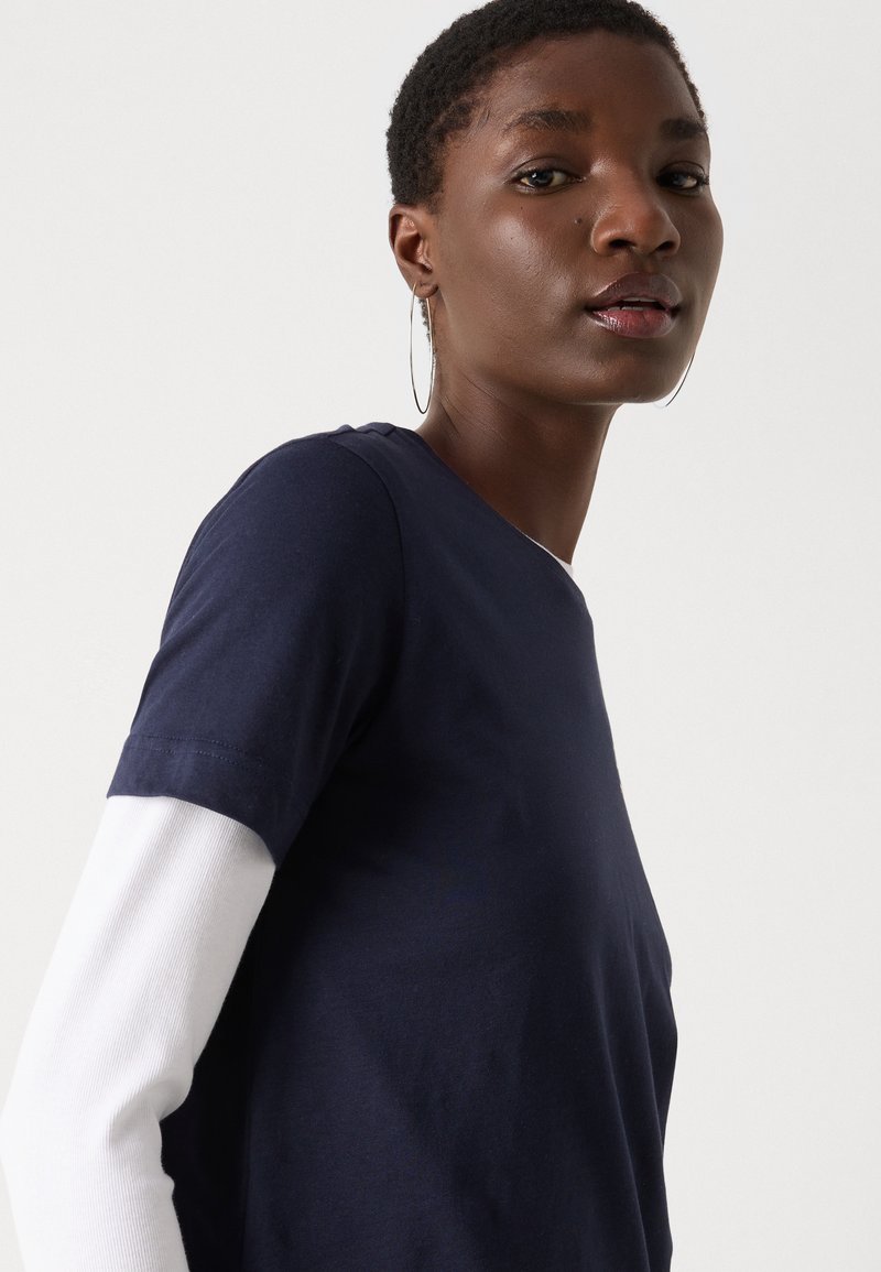 Granatowa koszulka z krótkim rękawem z białą warstwą z długim rękawem pod spodem. Gładki batonowy materiał, okrągły dekolt i detale na bocznych szwach.