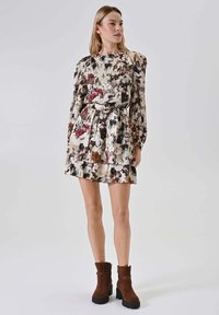 Vestito floreale con maniche lunghe, vita aderente e gonna a strati. Presenta uno sfondo crema chiaro con motivi floreali rosso scuro e verde.