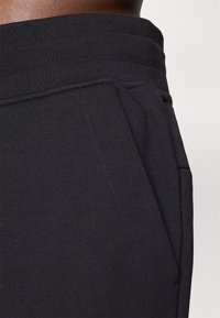 Joggers pretos de algodão com uma faixa na cintura canelada, bolsos laterais e detalhes de costura visíveis. Textura suave, design casual.