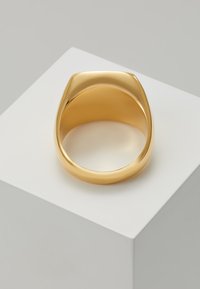 Guldring med et glat, afrundet design og en blank finish. Har en bred skæfte og en subtilt afslibning i toppen. Udstillet på en hvid pedestal.