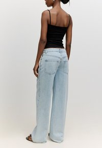 Hellblaue weit geschnittene Jeans mit einem klassischen Fünf-Taschen-Design, das eine subtile Waschung und eine lockere Passform aufweist, kombiniert mit einem schwarzen gerippten Tanktop.