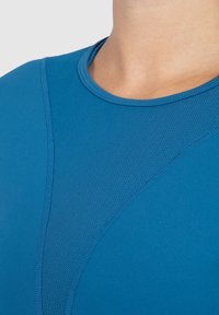 Blaues Sportshirt mit rundem Halsausschnitt, ausgestattet mit einem strukturierten Einsatz für Atmungsaktivität und glattem, dehnbarem Stoff für hohen Tragekomfort.
