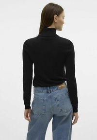 Črna turtleneck pulover s dolgimi rokavi, v kombinaciji z visokim pasom svetlo modrimi jeans hlačami, ki imajo na hrbtu rjav usnjen zaklop.