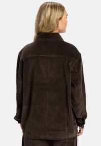 Brown corduroy jacket with a collar, visible seams, and a relaxed fit. The fabric features vertical ribbing and a slightly textured surface.