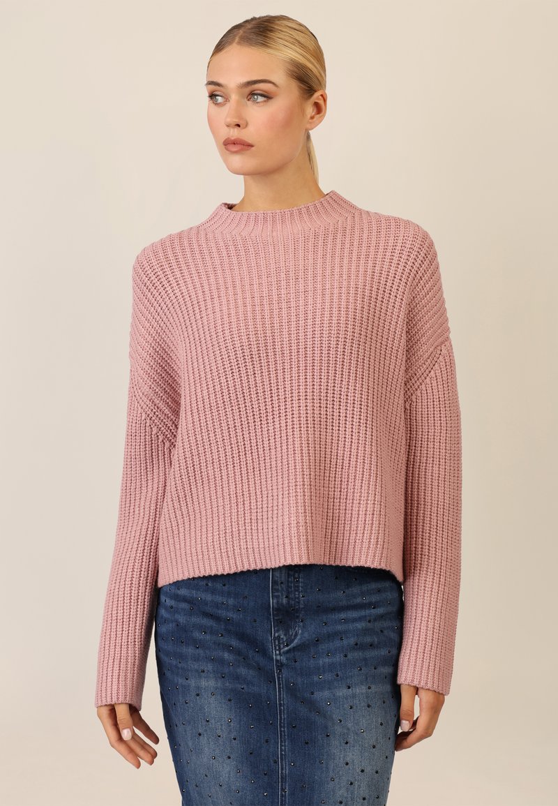 Light pink knitted sweater with a wide rib texture, round neckline, and cropped design. Paired with a denim skirt featuring small black studs.