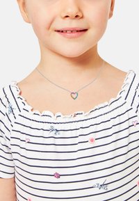 Collana d'argento con un pendente a forma di cuore decorato con pietre multicolori. Bambina che indossa una maglietta a righe bianche e blu navy con scollo a rouches.