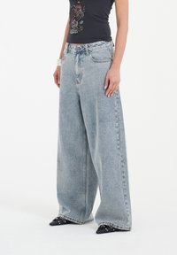 Jasnoniebieskie dżinsy z szerokimi nogawkami, wykonane z denimu, z wysokim stanem, przednimi kieszeniami i luźnym krojem, zestawione z czarnymi butami na szpic.