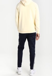 Světle žlutá mikina s prostornou kapucí, spárovaná s námořnickými sportovními kalhotami s bílými postranními pruhy a bílými teniskami.