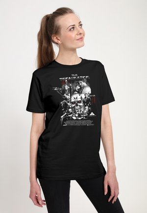 Kvinde iført sort t-shirt med The Terminator filmplakat grafik med karakterer og en robotisk kranium i sort, hvid og rød.