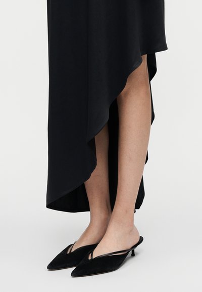Vestido preto assimétrico com textura suave, combinado com mules pretos de camurça com biqueira pontiaguda e design único de duas tiras.